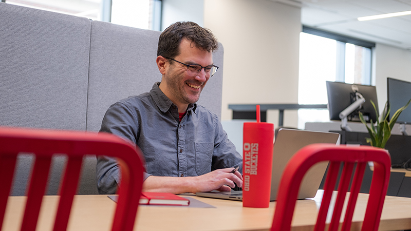 A laughing man looking at his laptop while sitting at a table