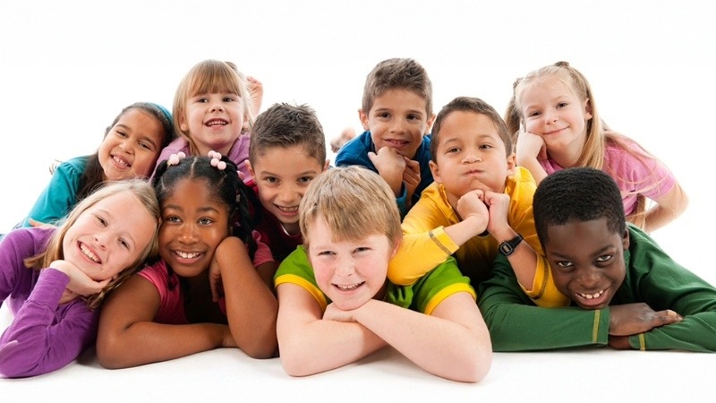 A group of smiling children lay on their arms and each other, posing for a picture.