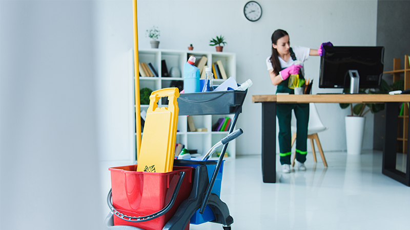 Woman cleaning a desk with cleaning products in the foreground