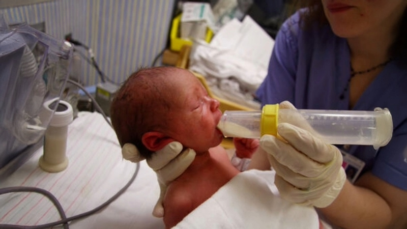 A newborn baby being bottle fed by a nurse inside of a hospital room.