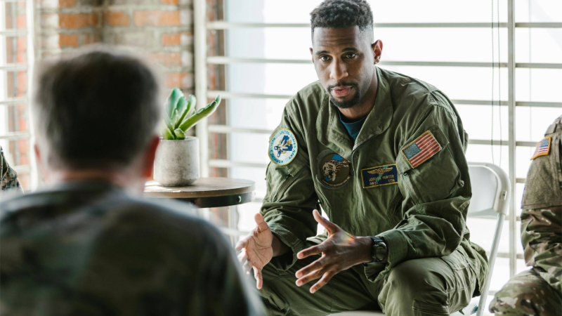 Man in slight suit speaks to group of uniformed military individuals.