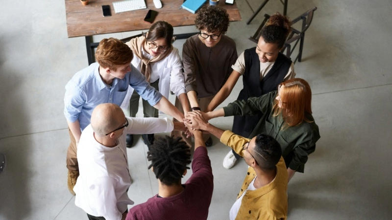 Eight people standing in a circle with hands stacked in the center, viewed from above.