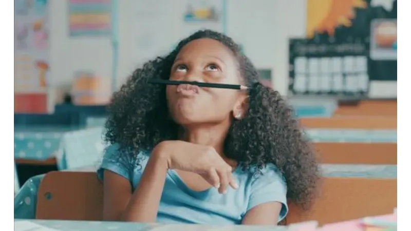 Young girl balancing a pencil on her lip distracted from work.